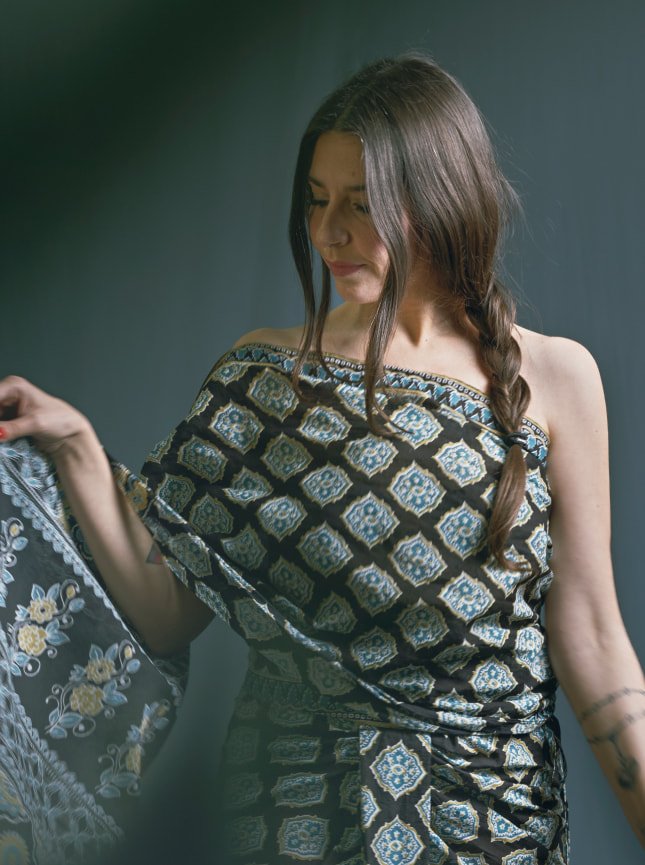 The black and blue block print wrap dress is worn here as a one shoulder wrap around dress. Wrapped to give an asymetric skirt with a central pleat the end of the dress that we refer to as the palu is draped over the left shoulder. It can be pinned in place or left free.
