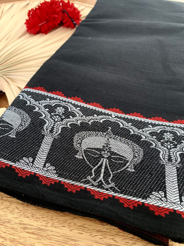 A close up of the embroidered border on the ByGungur Anjali Saree. The black saree has a white stitched border featuring the face of an Indian classical dancer with her hands in Anjali mudra. Around the dancer is a motif representing the architecture of temples of Orissa, India. The white stitched border is highlighted with a repeating red gemoetric pattern. The Anjali saree is perfect to use as a practice saree for Indian classical dance or for any formal occasion.