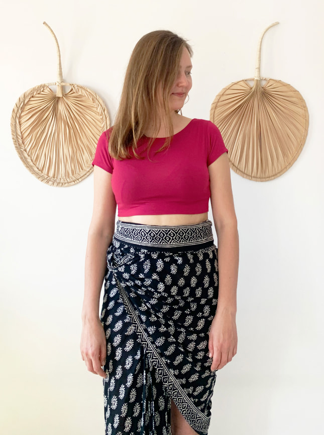 The Pearl Crop is a reversable crop top. Here the model is wearing it with the cutaway V at the back and a high round neckline at the front. She's wearing the orquidea red crop top teamed with the ByGungur Block Print Wrap skirt in black and white