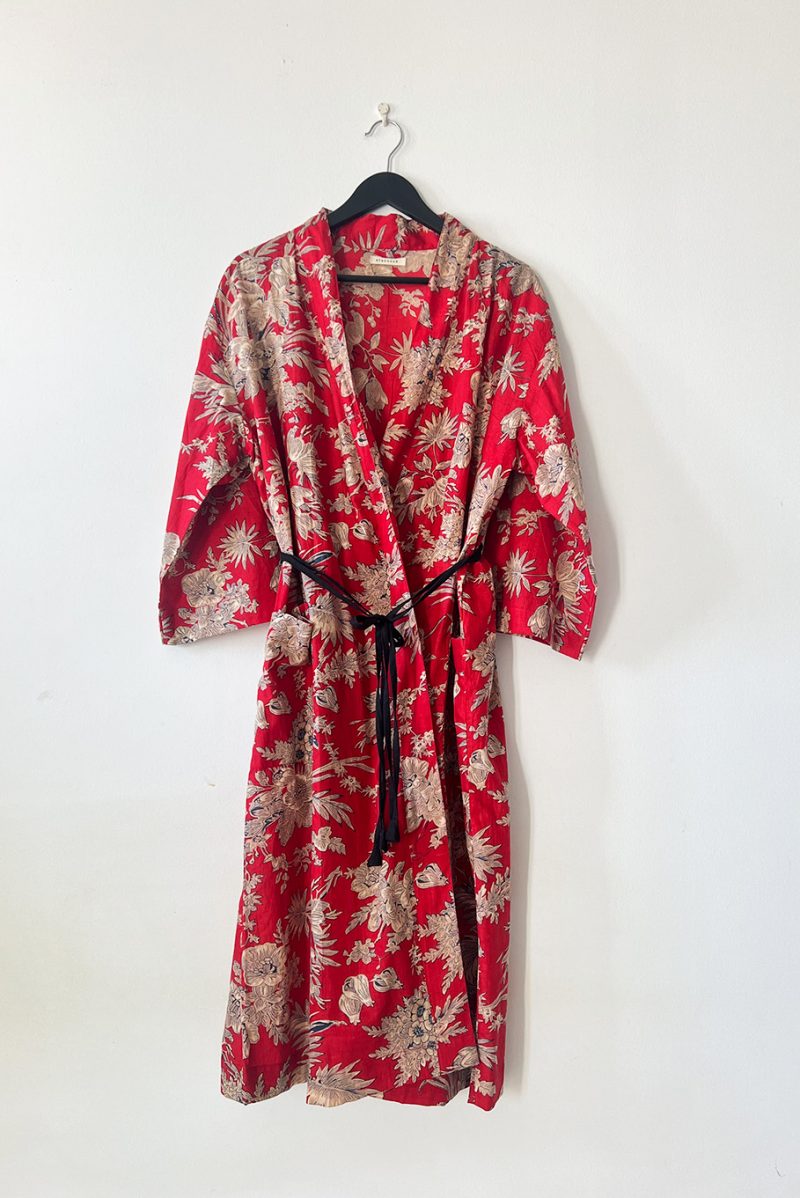 Lily Kimo Red on the hanger. This floral print kimono is made of 100% cotton. The design is of cream floral print on a red background. It has two poockets and a black adjustable belt attached at the back.